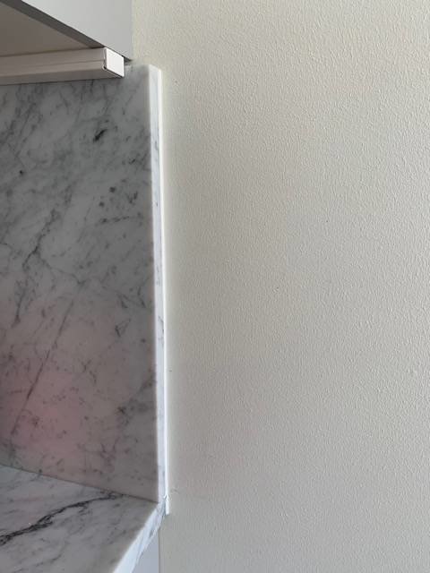 Väggkant vid köksskåp där marmorskivor sticker ut, skapar ojämn yta inför tapetsering.