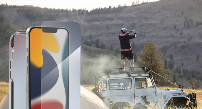 Person står på taket till en terrängbil i naturen och fotograferar medan solen går ner, bredvid visas skyddade smartphones.