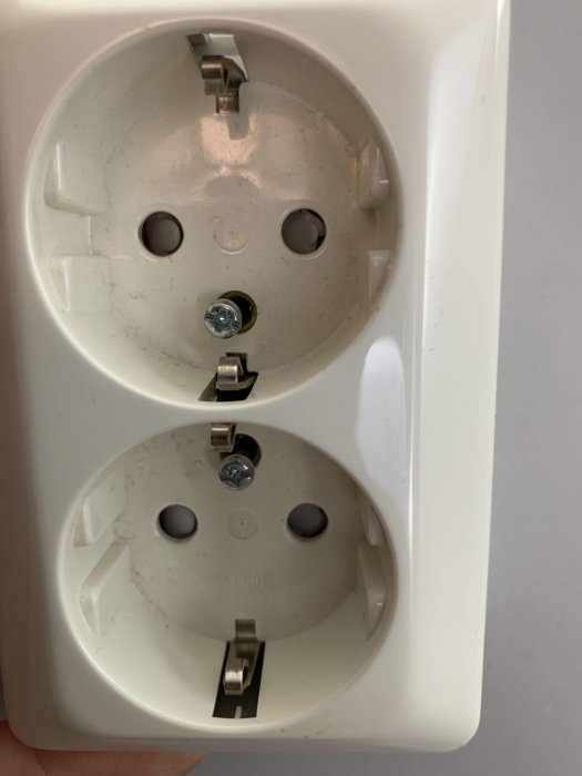 Ett vägguttag med två skruvar lossade, redo för demontering.