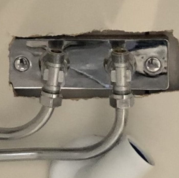 Dubbel vattenanslutning för handfat synlig genom en väggöppning.