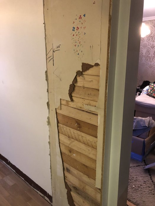 Partial view of a non-load-bearing wall removed revealing wooden planks, next to intact wallpapered wall.