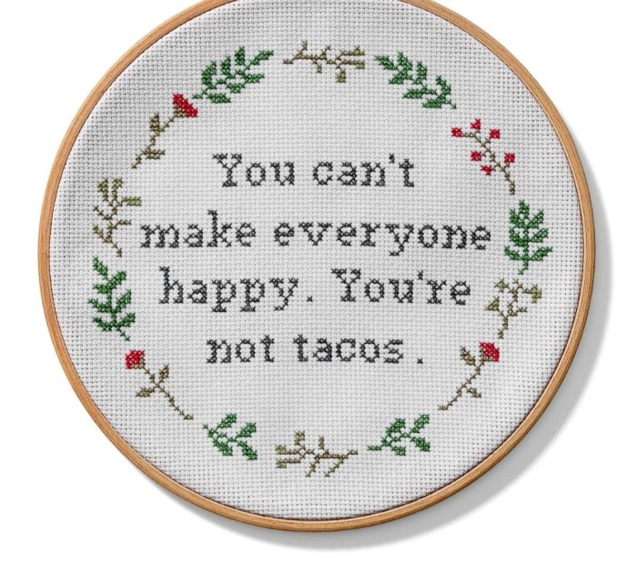 Broderi i båge med texten "You can't make everyone happy. You're not tacos." och dekorativa gröna blad samt röda blommor.