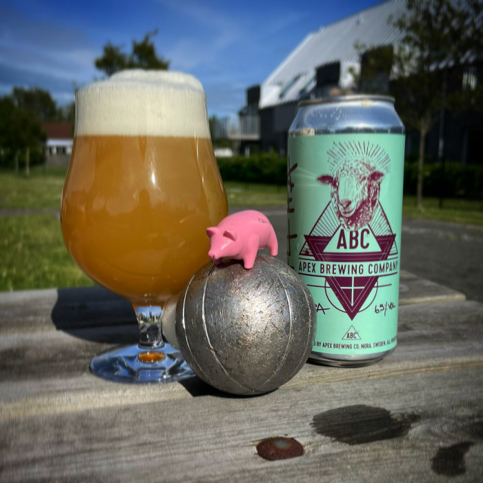 En rosa leksaksgalt på en metallboll, intill ett glas öl och en ölburk från Apex Brewing.