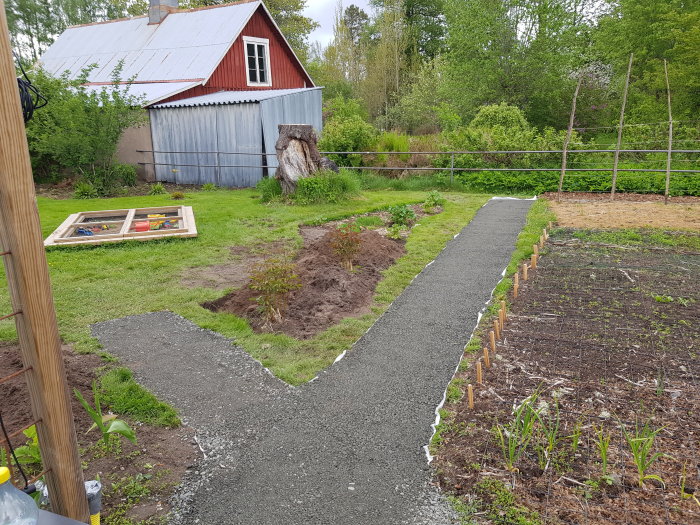 Nygrävd grusgång med 0-16 kross bredvid en trädgård och ett rött hus.