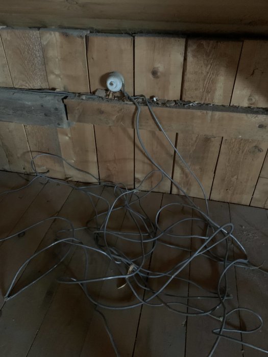 Hopkurad gammal kabel av bly avklippt vid ena änden, andra änden sitter i en vit dosa på en övervåning under renovering.