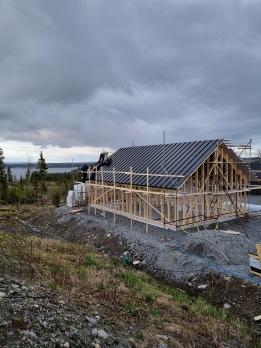 Halvfärdig takläggning på en nybyggd stomme till ett hus med en grå himmel i bakgrunden.