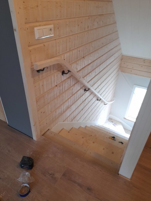 Trappa med vitmålat räcke och väggpanel i trä under renovering.