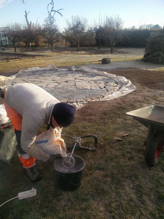 Person fogar skifferstenar på en rund uteplats med cement under solig himmel.