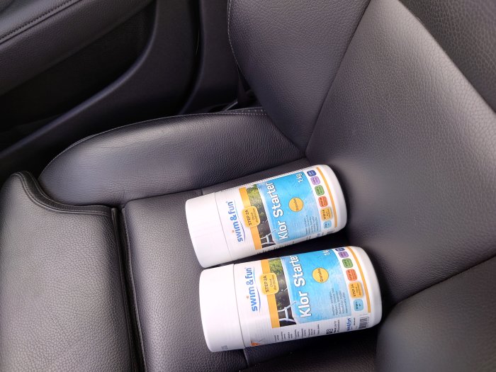 Två flaskor med klorstarters för pool på svart bilinredning.