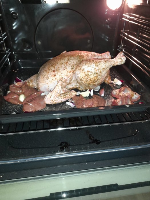 Hel kyckling kryddad i ugnen, omgiven av vitlöksbitar och okänt kött.