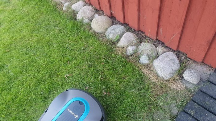 Robotgräsklippare stoppad vid stenrad och träplank längs gräsmatta.