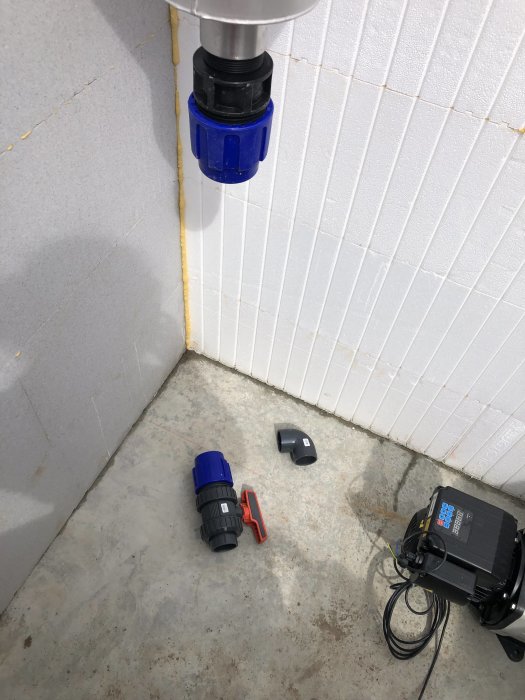 Klumpig VVS-koppling på vägg, lösa delar och verktyg på betonggolv i ett byggprojekt.