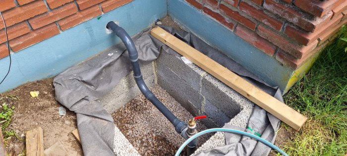 Rörinstallation vid husgrund med kopplade rör och kran för vattensystem.