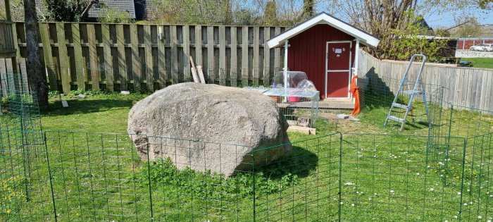 Stor slät sten på tomt som blockerar bygge med röd skjul och steg i bakgrunden.