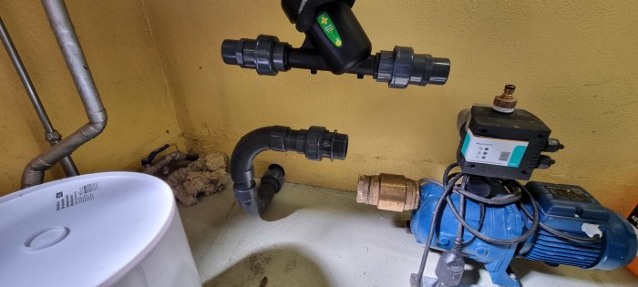 VVS-installation med flödesvakt, pump, filter och kulventiler i ett garage.