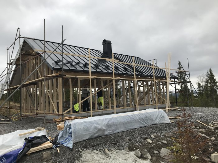 Nyligen färdigställt hus med tak och hängrännor, omgivet av ställningar och virke på marken.