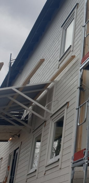Utvändig vy av ett hus med en monterad dekorationslist under takfoten där en slang kommer ut vid sidan av en byggnadsställning.