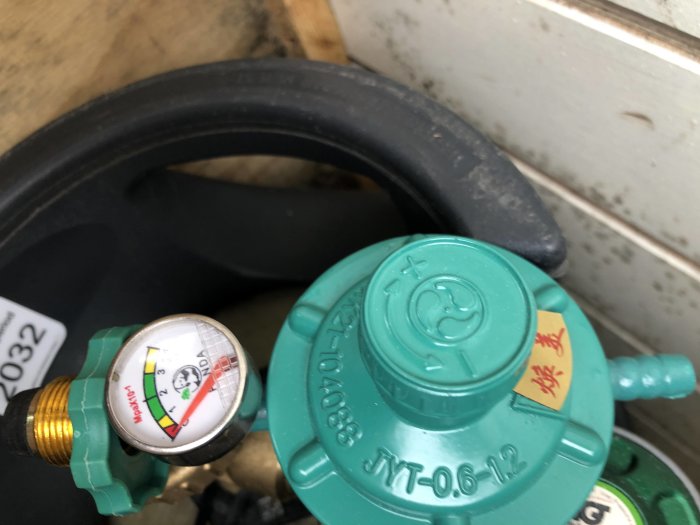 Grön gasregulator med tryckmätare kopplad till en gasbehållare.