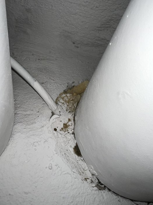 Uppskuret rör och kabel i hörnet av ett vitmålat tak, med synliga tecken på skador eller läckage.