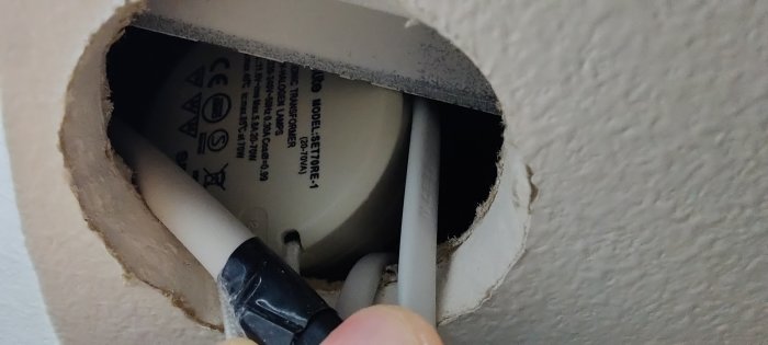 En hand som pekar på en gömd elektrisk transformator bakom en rund väggöppning.