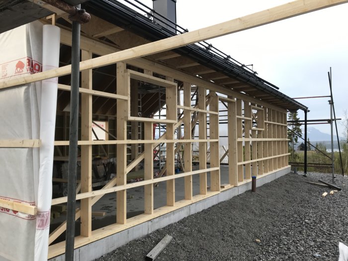 Hus under konstruktion med korsregling, isolering, vindduk och delvis spikläkt på fasaden.