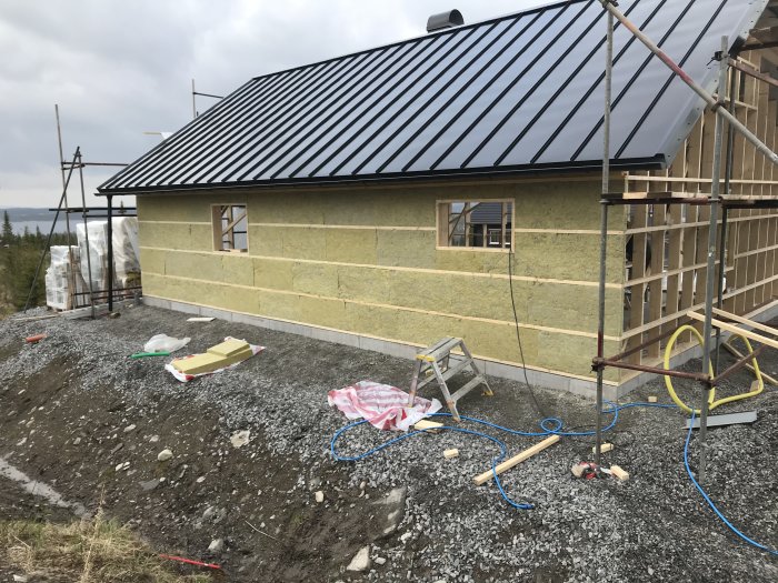 Hus under renovering med isolering och vindduk, halvfärdigt tak och material på marken.