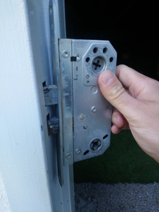 En hand håller en öppen lucka med en synlig gammal assa evo 310 låsenhet, problem med passform noteras.