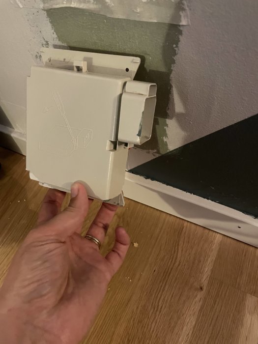 Hand håller en öppen eluttagsdosa framför ett hål i väggen med synliga kablar.