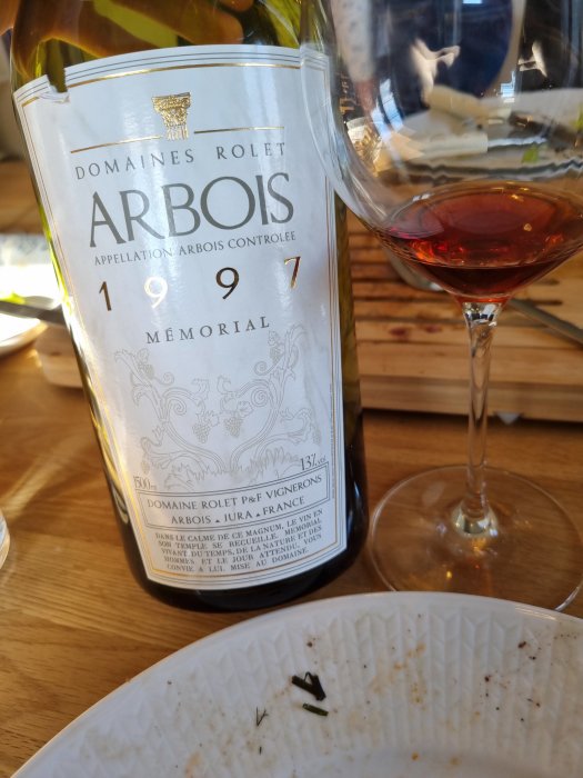 Flaska av Domaine Rolet Arbois vin från 1971 bredvid ett vinglas, på ett bord med tom tallrik.