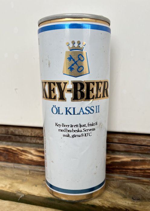 Ölburk av märket "KEY-BEER ÖL KLASS II" med textbeskrivning och värmetips på träbänk.