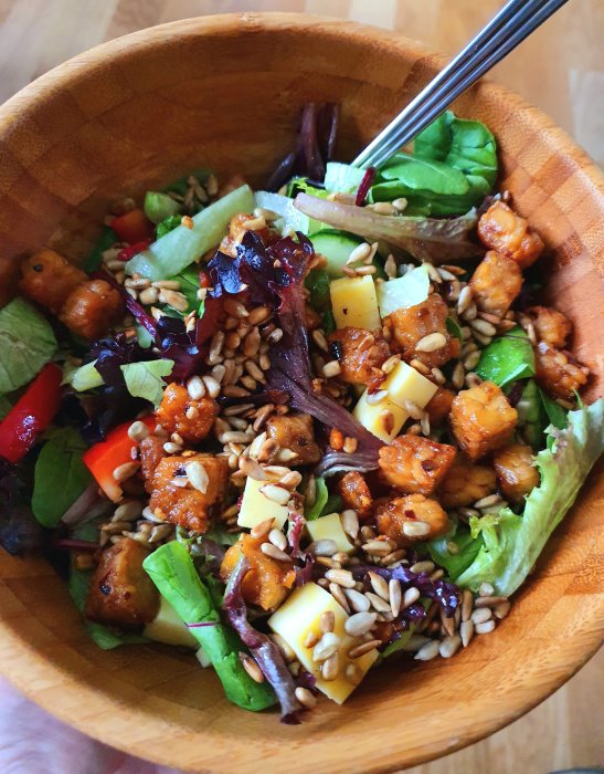 Färgrik sallad med vego-ost, stekt tempeh, rostad solrosfrön i en träskål.