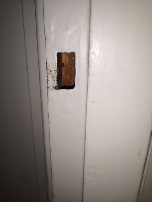 Närbild på en vitmålad dörrkarm med urgröpning för låset där ett tjockt färglager syns.