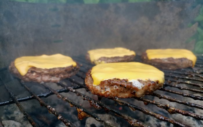 Högrevsburgare med smält cheddarost på grillen omgivna av rök.