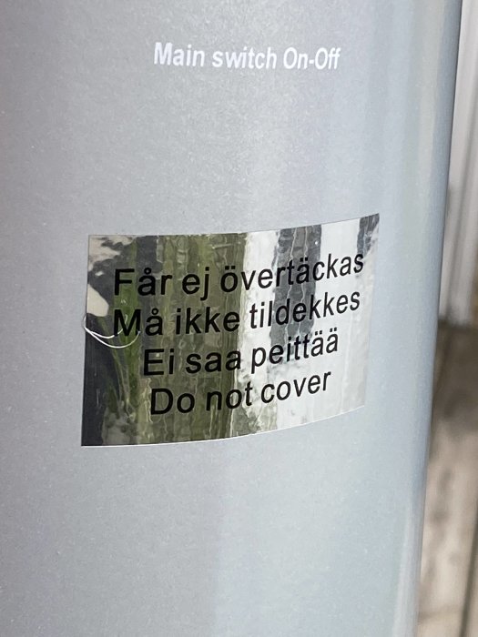 Textetikett med varning "Får ej övertäckas / Må ikke tildekkes / Ei saa peittää / Do not cover" på en apparat.