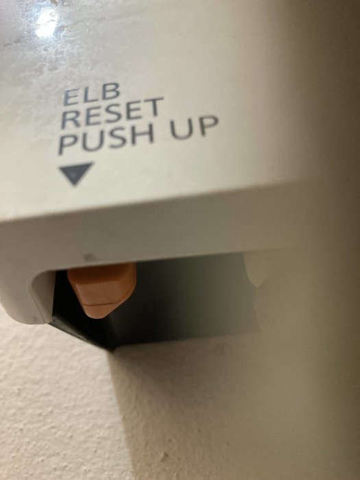 Närbild på en vattenvärmare med texten "ELB RESET PUSH UP" och en synlig orange knapp.