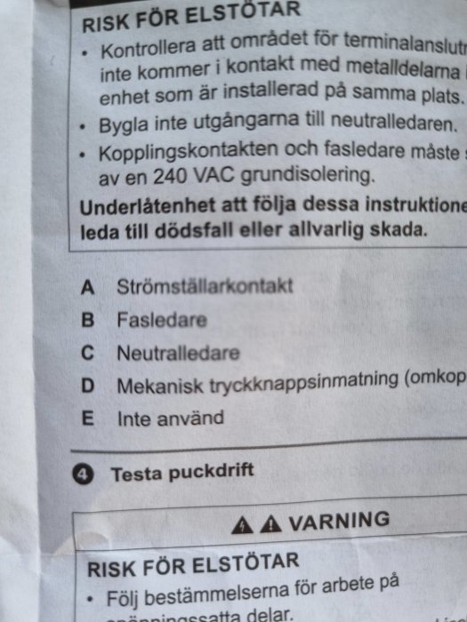 En närbild på en installationsguide med varningar och instruktioner för elanslutningar som ska kopplas.