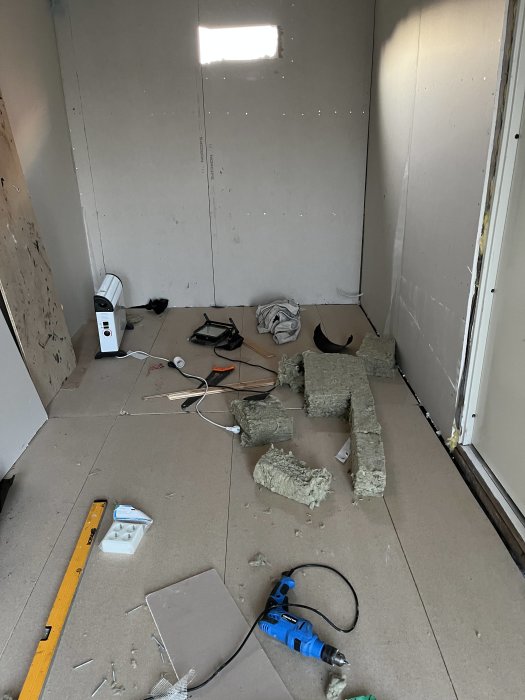 Inre del av en gäststuga under byggnation med isoleringsmaterial på golvet och obehandlade gipsskivor på väggarna.