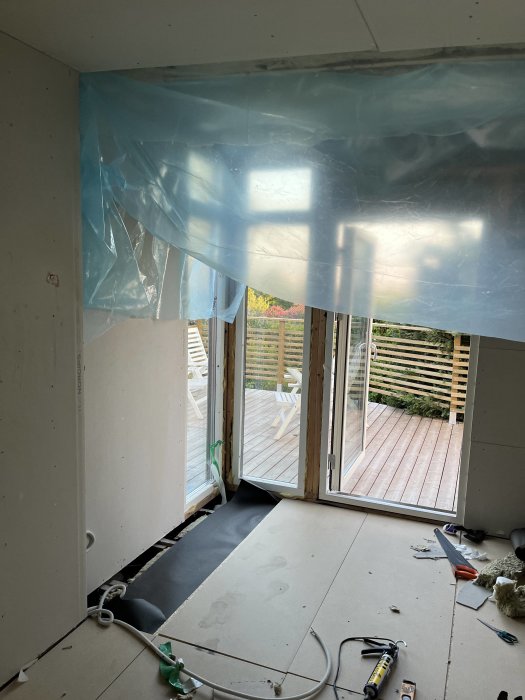 Byggarbetsplats inuti gäststuga under konstruktion med plast i taket och verktyg på golvet.