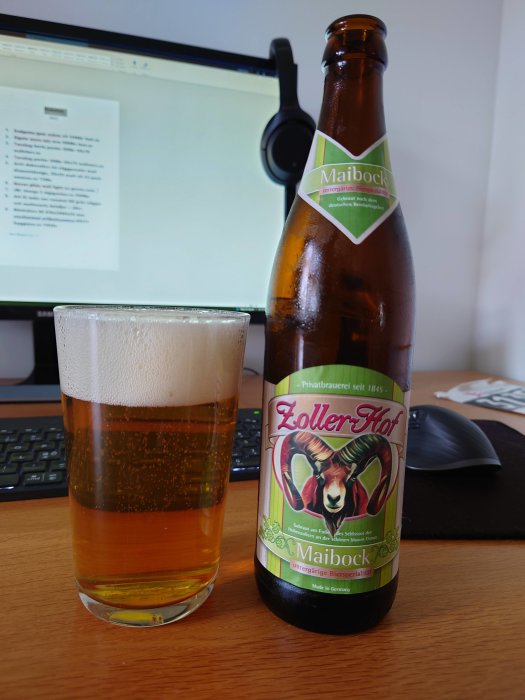 Flaska och glas med Maibock öl framför en datorskärm och ett headset.