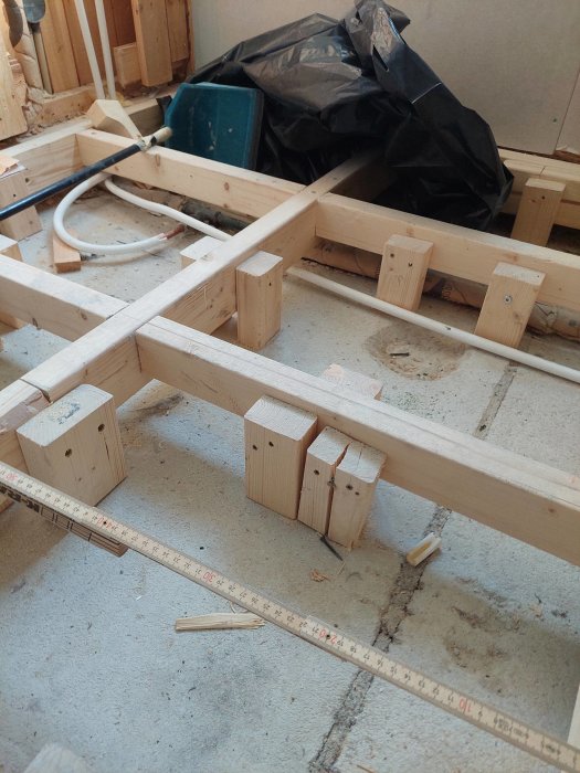 Delvis konstruerat träregelverk i pågående badrumsrenovering med mätsticka och avstödningsklossar.