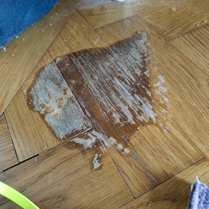 Parkettskada från utspilld målarfärg med bortdragen färg och synliga fläckar.