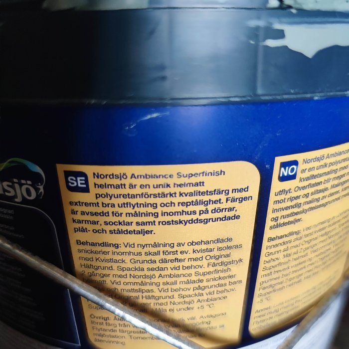 Välvd målarburk med blå färg som har läckt på en mörk bakgrund, detalj av etiketten synlig.