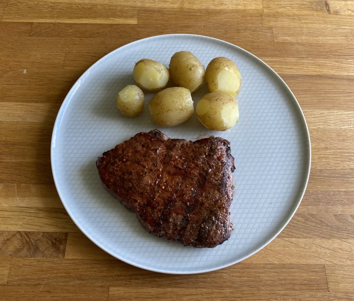 Grillad rostbiff och färskpotatis på en vit tallrik mot en träbakgrund.