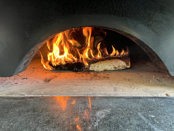 Brinnande ved i en traditionell pizzaugn, redo för pizzabakning.