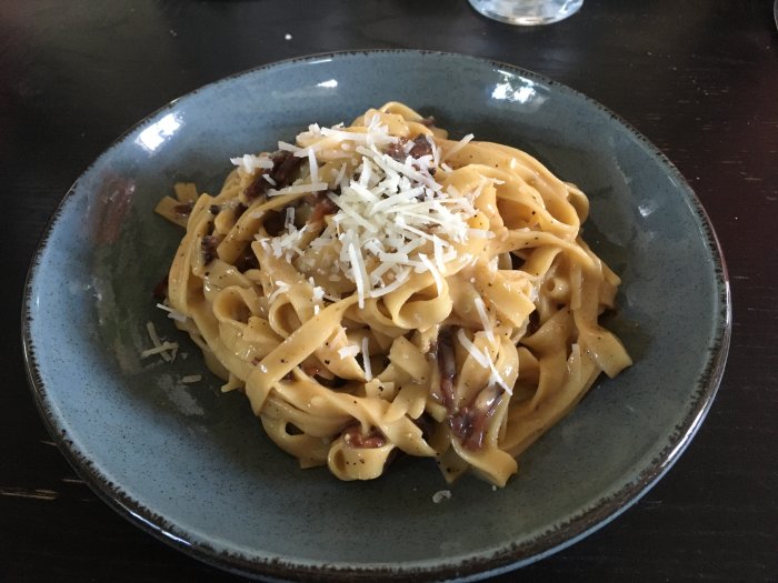 Tallrik med traditionell pasta carbonara toppad med riven pecorinoost.
