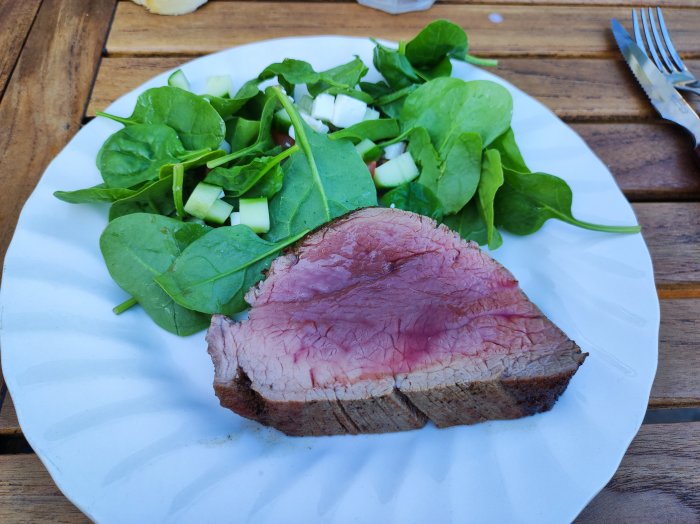 Rosastekt köttbit på tallrik med spenat- och gurksallad.