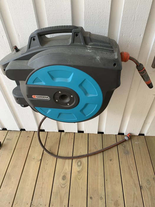 Trädgårdsslangvinda från Gardenia monterad på vit vägg med utdragen slang.
