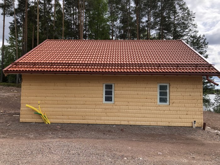 Nybehandlad fasad med järnvitriol på trähus med rött tak, två fönster, omgivet av natur.