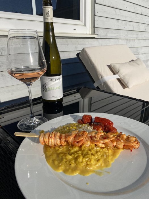 Risotto milanese med räkor och grillade tomater serverad på tallrik med rosévin och flaska på utomhusbord.