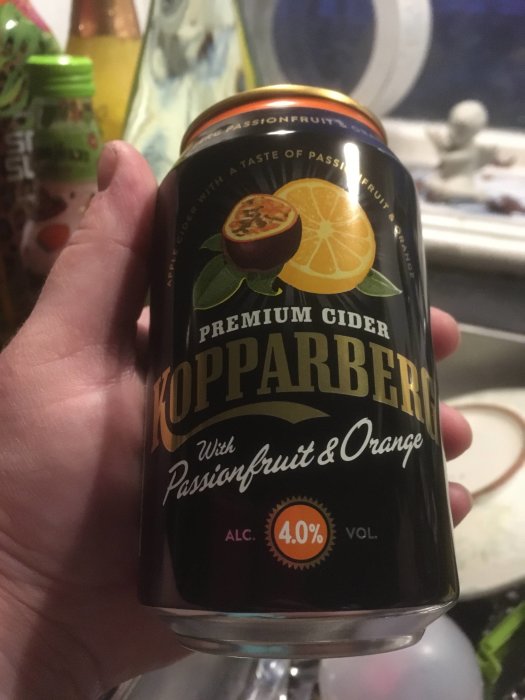 Hand håller en burk Kopparberg Premium Cider med passionfrukt och apelsin, 4,0 % alkohol.